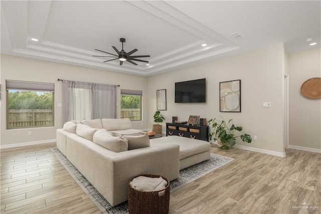 living room featuring ceiling fan, light hardwood / wood-style floors, and a tray ceiling