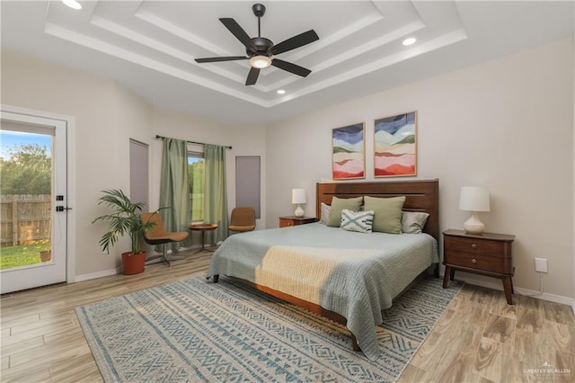 bedroom with access to exterior, ceiling fan, a raised ceiling, and light hardwood / wood-style flooring