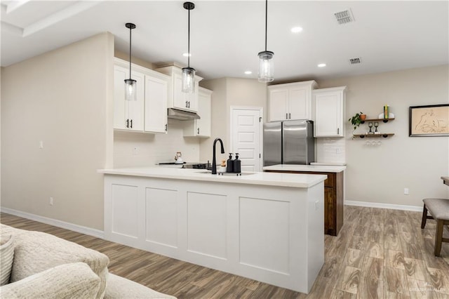 kitchen featuring white cabinets, sink, hanging light fixtures, stainless steel fridge, and light hardwood / wood-style floors