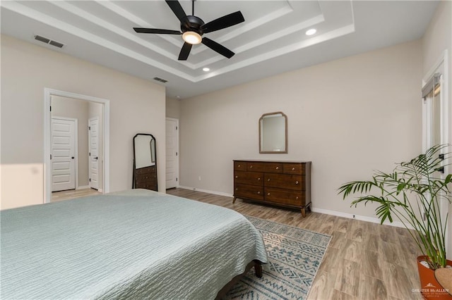 bedroom featuring a tray ceiling, ceiling fan, and light wood-type flooring