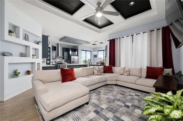 living room with a raised ceiling, ceiling fan, built in features, and light hardwood / wood-style floors