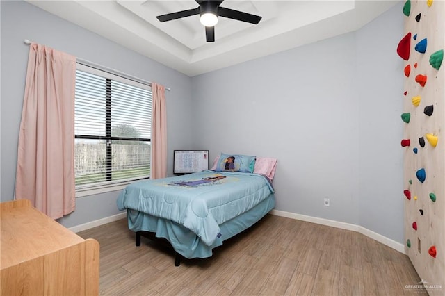 bedroom with light wood-type flooring, a tray ceiling, and ceiling fan