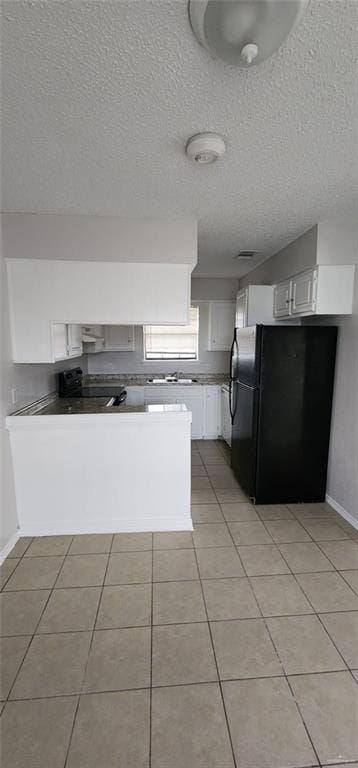 kitchen featuring white cabinets, a textured ceiling, black fridge, and light tile patterned flooring