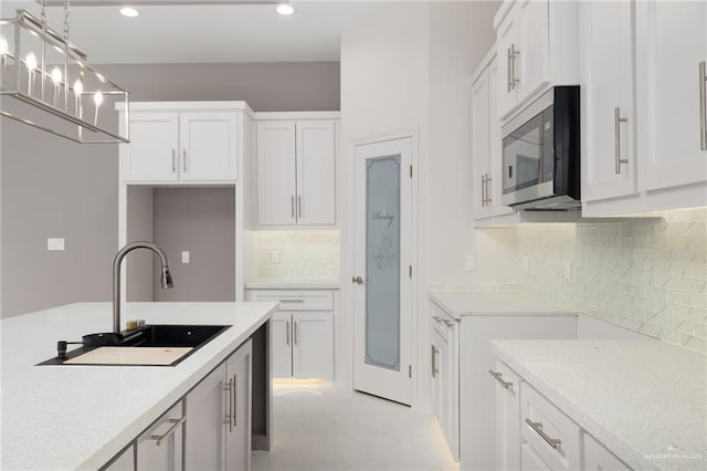 kitchen featuring light stone countertops, sink, hanging light fixtures, tasteful backsplash, and white cabinets