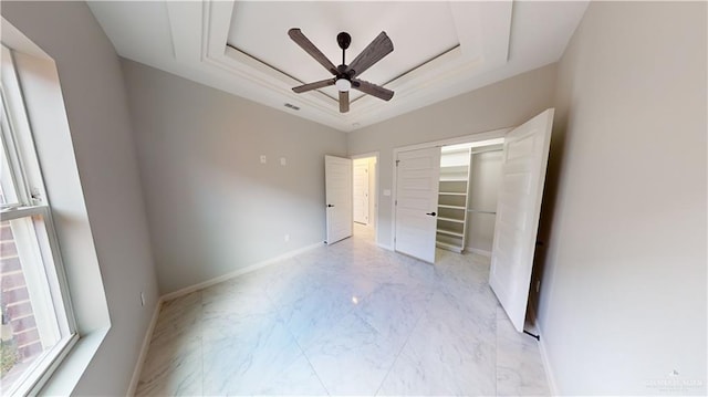 unfurnished bedroom with ceiling fan, a tray ceiling, and a closet