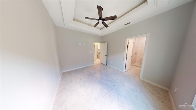 unfurnished bedroom with a raised ceiling, ensuite bathroom, and ceiling fan