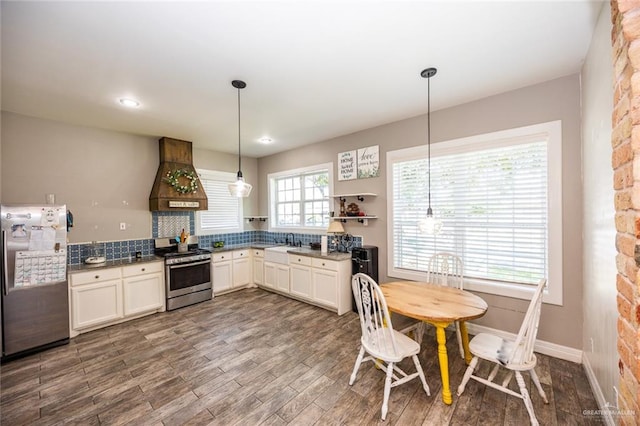 kitchen featuring hanging light fixtures, backsplash, wood-type flooring, appliances with stainless steel finishes, and custom exhaust hood