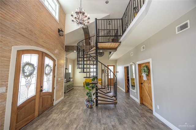 foyer with french doors, a towering ceiling, a notable chandelier, and hardwood / wood-style floors