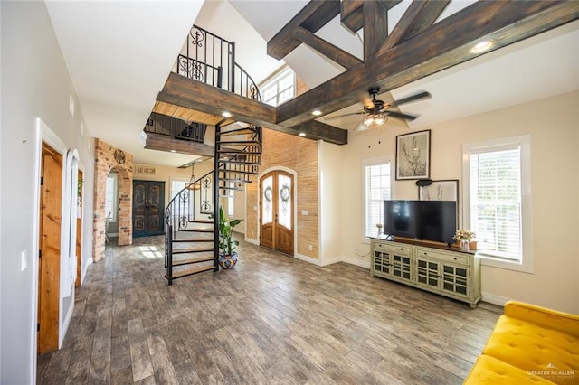 unfurnished living room featuring ceiling fan, beam ceiling, wood-type flooring, and a towering ceiling