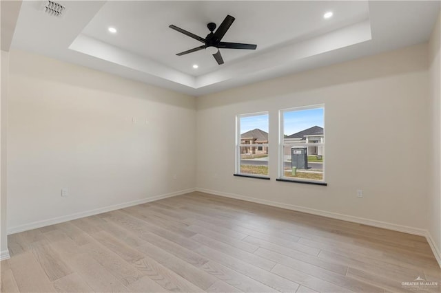 unfurnished room featuring ceiling fan, light wood-type flooring, and a tray ceiling