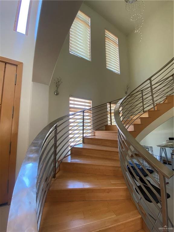 staircase with a chandelier, wood-type flooring, and a towering ceiling