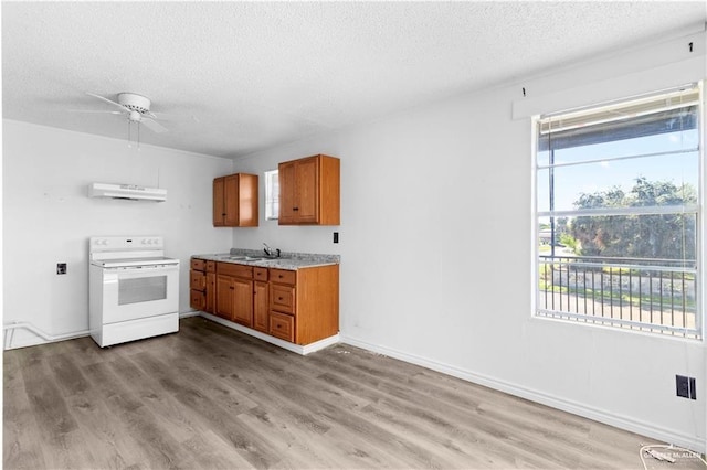 kitchen with a textured ceiling, under cabinet range hood, brown cabinetry, white electric range oven, and a sink