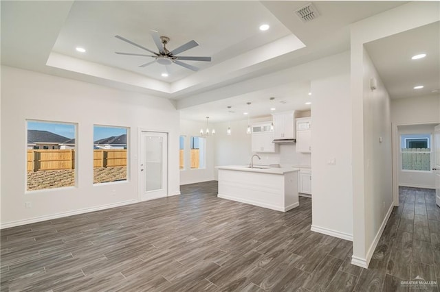 unfurnished living room featuring visible vents, a raised ceiling, dark wood-style flooring, and ceiling fan with notable chandelier