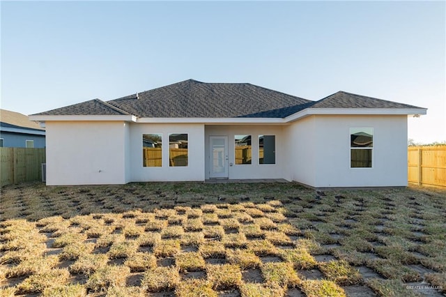 back of house featuring roof with shingles, fence, a lawn, and stucco siding