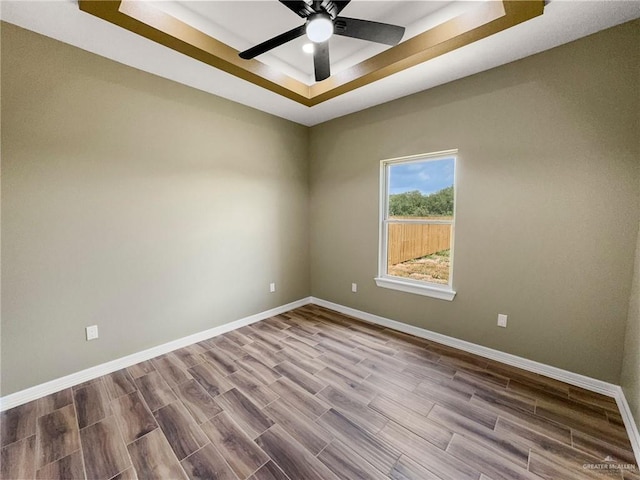 empty room featuring ceiling fan, a raised ceiling, and wood-type flooring