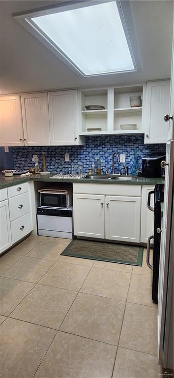 6201 Padre Blvd Unit 308, South Padre Island, TX 78597 - kitchen with backsplash, open shelves, stainless steel microwave, white cabinetry, and dark countertops