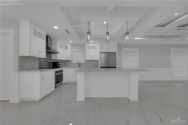 kitchen featuring wall chimney exhaust hood, stainless steel appliances, white cabinets, a center island, and hanging light fixtures