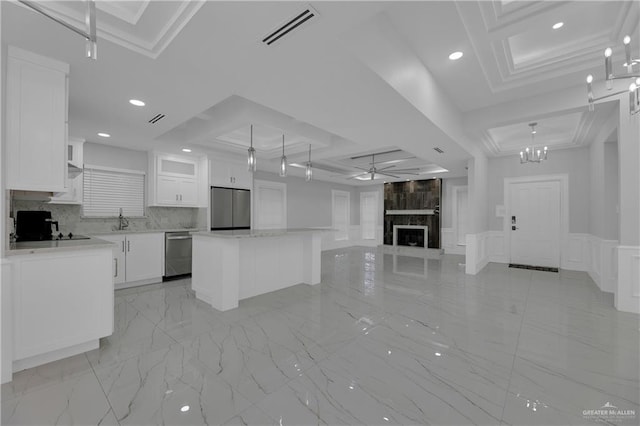 kitchen with stainless steel appliances, a kitchen island, a raised ceiling, a fireplace, and white cabinets