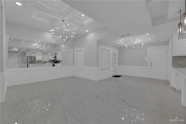 unfurnished living room featuring a chandelier, a raised ceiling, coffered ceiling, and crown molding