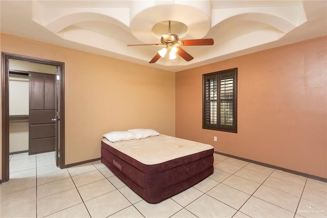 bedroom with a raised ceiling, light tile patterned flooring, baseboards, and ceiling fan