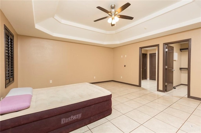 unfurnished bedroom with a tray ceiling, a walk in closet, ceiling fan, and light tile patterned floors