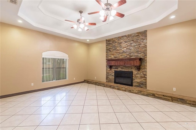 unfurnished living room with a raised ceiling, ceiling fan, a fireplace, and light tile patterned floors