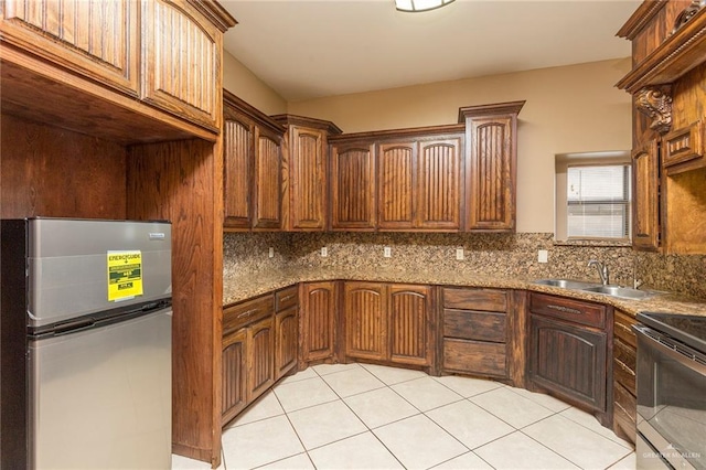 kitchen with backsplash, sink, dark stone countertops, appliances with stainless steel finishes, and light tile patterned flooring