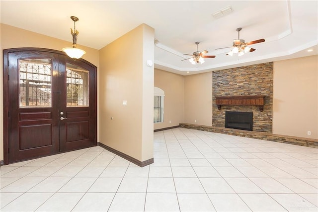 foyer featuring a raised ceiling, ceiling fan, a fireplace, and light tile patterned flooring