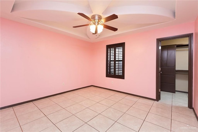 unfurnished room with light tile patterned flooring, a ceiling fan, a raised ceiling, and baseboards