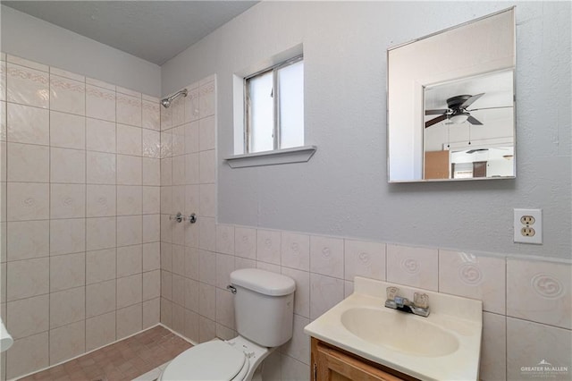 full bathroom with tile walls, toilet, ceiling fan, a tile shower, and vanity