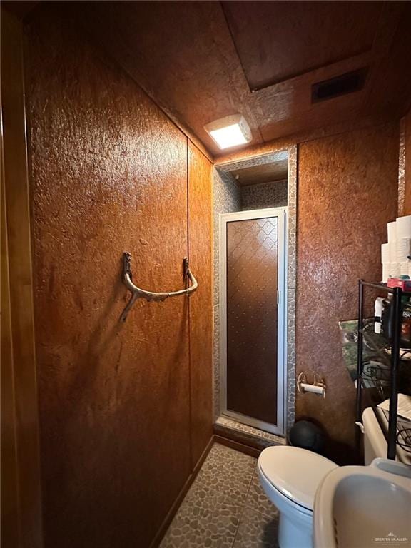 bathroom featuring sink, toilet, a shower with shower door, and wood walls