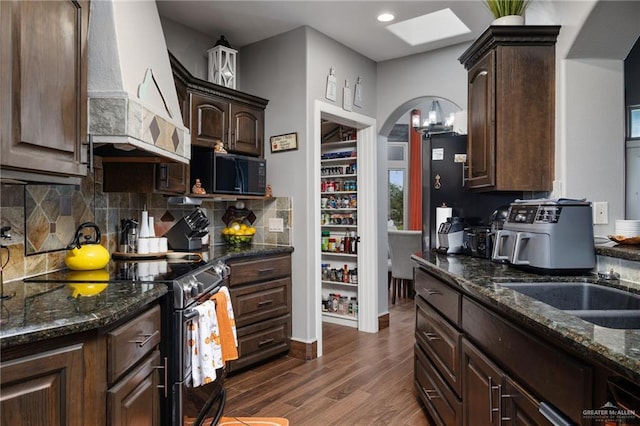 kitchen featuring dark hardwood / wood-style flooring, dark stone countertops, dark brown cabinets, stainless steel range with electric cooktop, and custom range hood