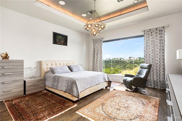 bedroom with a notable chandelier, dark wood-type flooring, and a tray ceiling