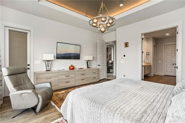 bedroom with a notable chandelier, a raised ceiling, dark wood-type flooring, and connected bathroom