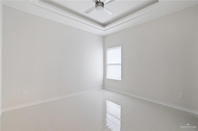 empty room featuring baseboards, a ceiling fan, light tile patterned floors, and a tray ceiling