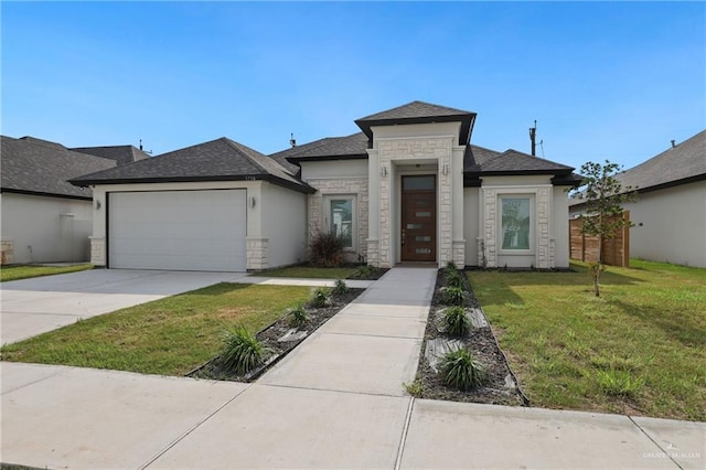 prairie-style house with an attached garage, a shingled roof, stone siding, a front yard, and concrete driveway