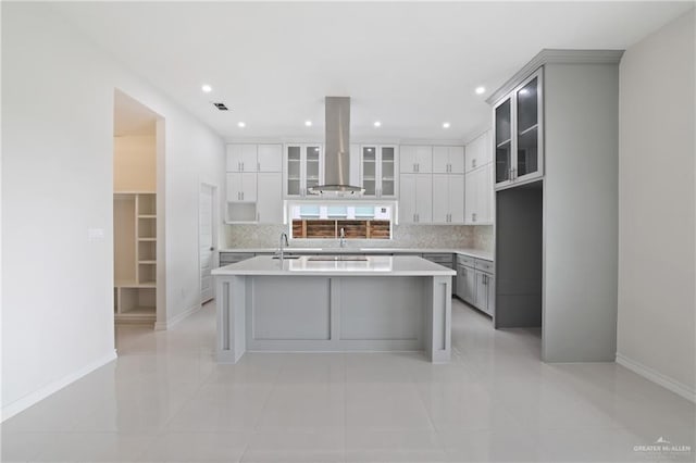 kitchen with backsplash, baseboards, an island with sink, and island exhaust hood