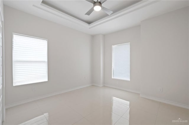 spare room with ceiling fan, plenty of natural light, baseboards, and a raised ceiling
