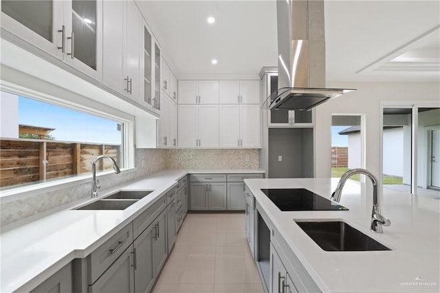 kitchen featuring wall chimney range hood, tasteful backsplash, black electric cooktop, gray cabinetry, and a sink