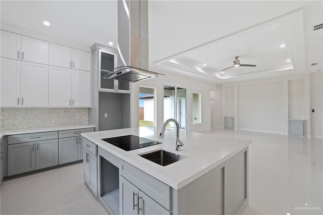 kitchen featuring light tile patterned flooring, black electric stovetop, island range hood, a raised ceiling, and a sink