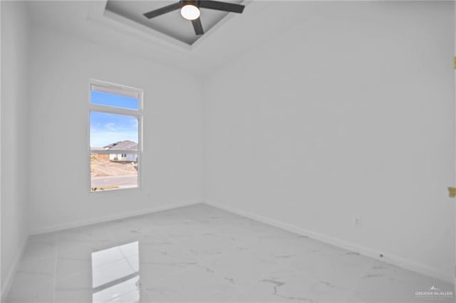 spare room featuring a tray ceiling, marble finish floor, and baseboards