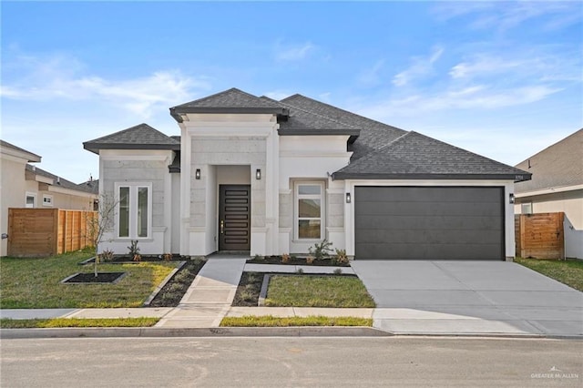 prairie-style home featuring a shingled roof, concrete driveway, fence, a garage, and a front lawn