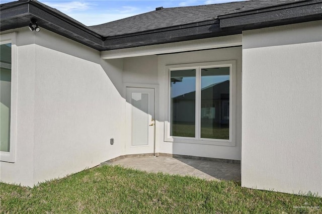 exterior space featuring stucco siding, a patio area, a yard, and roof with shingles