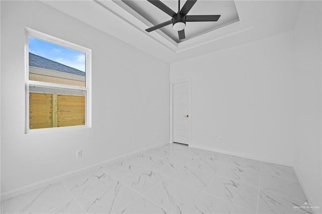 spare room featuring marble finish floor, baseboards, a tray ceiling, and a ceiling fan