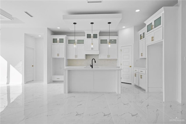 kitchen featuring glass insert cabinets, white cabinetry, decorative light fixtures, and an island with sink