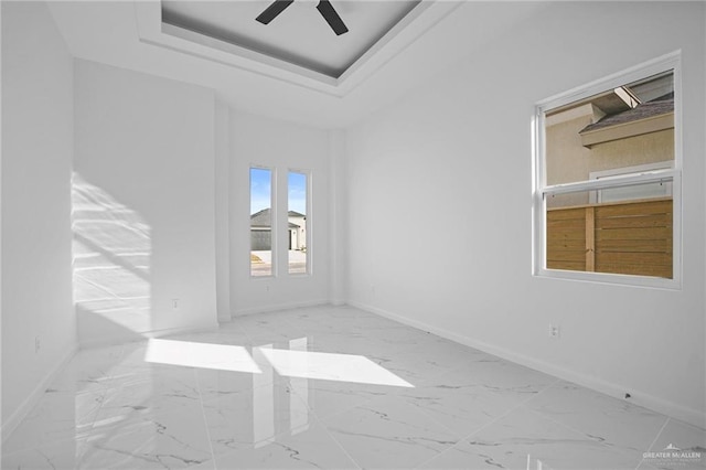 unfurnished room featuring marble finish floor, baseboards, a raised ceiling, and a ceiling fan