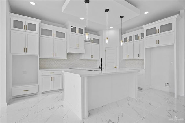 kitchen featuring glass insert cabinets, light countertops, white cabinetry, and a center island with sink