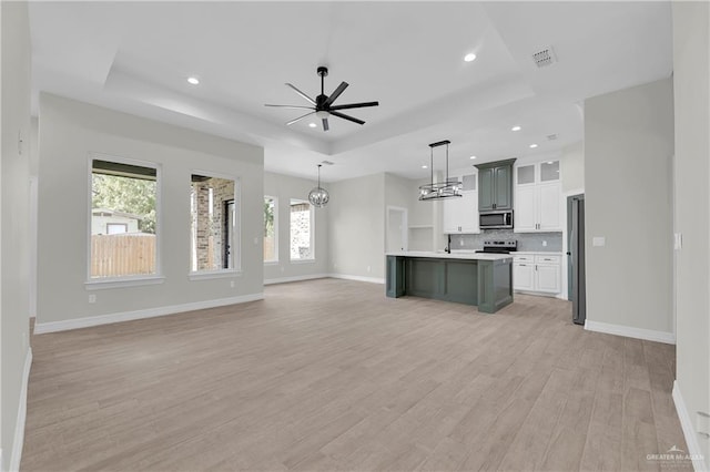 kitchen with open floor plan, light countertops, appliances with stainless steel finishes, light wood-type flooring, and a tray ceiling