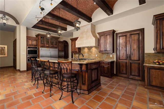 kitchen with hanging light fixtures, stainless steel appliances, backsplash, dark brown cabinets, and custom range hood