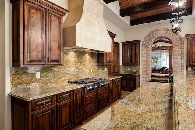 kitchen with custom exhaust hood, light stone countertops, decorative backsplash, and stainless steel gas cooktop